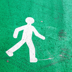 Piktogramm eines gehenden Männchens auf grünem Asphalt