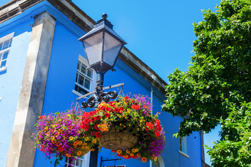 Fototapeta na wymiar Straßenlaterne mit Blumenkörben vor einem blauen Haus in Glastonbury, England