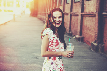 pretty laughing girl with milk shake walking at morning street