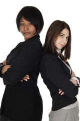 Two women stand back to back looking at viewer.