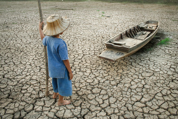 Boy looking to wooden boat on cracked earth.