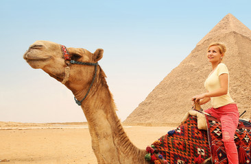 Tourist riding camel in Giza. Young blonde woman near Pyramid of