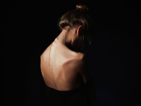 young woman with naked back over black background.sad girl