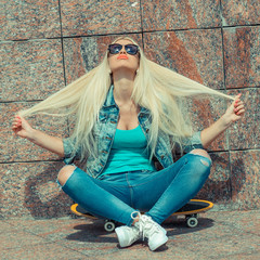 Young trendy girl in jacket sitting on a skateboard on the background of  wall. Outdoor lifestyle portrait
