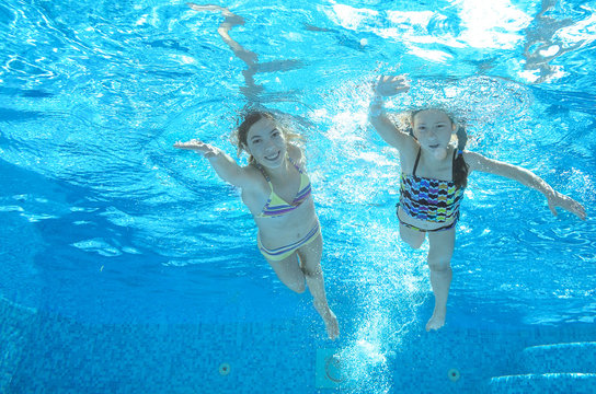 Children swim in pool underwater, happy active girls have fun in water