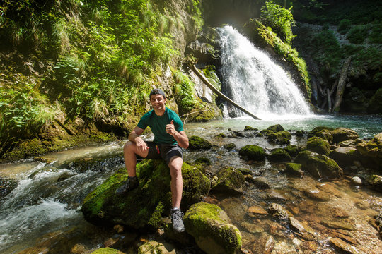 Man showing thumbs up sign outdoor near a waterfall