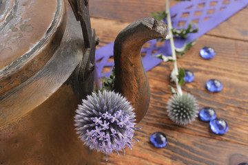Rustikaler Kupferkessel auf alten Holzdielen mit blauen Disteln und blauen Glassteinen dekoriert