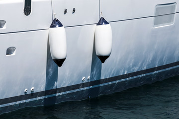 Small ship fenders hanging above white yacht hull