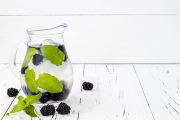 Healthy detox water with blackberry and mint. Cold refreshing berry drink with ice on white wooden table. Copy space background