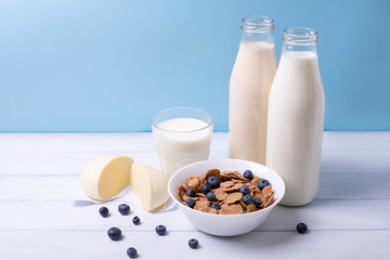 Front view of fresh dairy products and cereals with blueberries on a white wooden table and blue background. Shallow depth of field