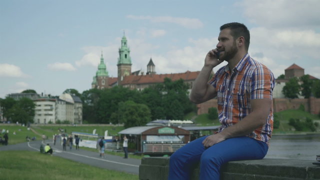 Man sitting on wall and talking by smartphone.
