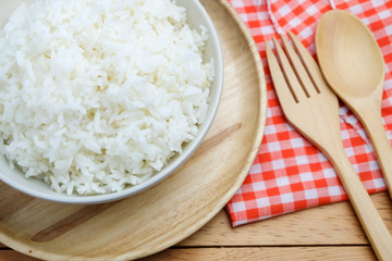 bowl full of rice in plate and spoon on wood