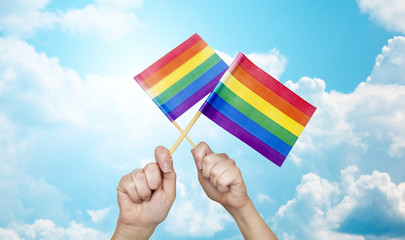hands holding rainbow flags over sky background
