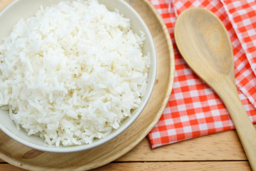 bowl full of rice in plate and spoon on wood