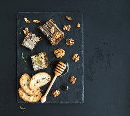 Honeycomb, walnuts, bread slices and honey dipper on black slate