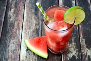 Watermelon lime water in a glass with melon slice and straw against rustic wood background