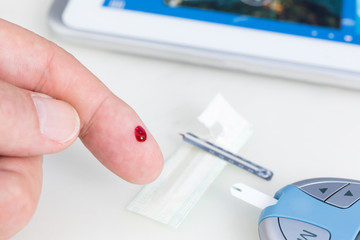 Mann mißt  Blutzucker, im Hintergrund ein Tablet PC, Diabetes m