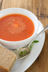 tomato soup in white bowl with sandwich on brown wooden background
