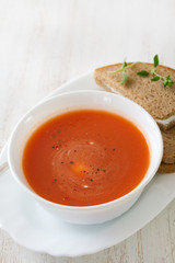 tomato soup in white bowl with sandwich on white wooden background