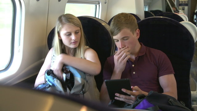 Teenage Couple Using Digital Devices On Train Journey
