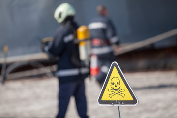 danger sign with skull and crossbones, firefighters on background