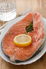 fresh salmon with lemon on white dish and glass of water on brown wooden background