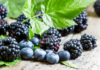 Fresh blackberries and blueberries with leaves on the old wooden