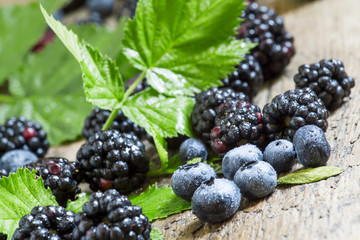 Fresh blackberries and blueberries with leaves on the old wooden