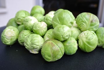 Fototapeta premium Pile of fresh green raw Brussels sprouts on the black table. Healthy/clean eating concept; organic/unprocessed food; paleo diet.
