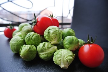 Pile of fresh green Brussels sprouts and red cherry tomatoes on the black table. Healthy/clean eating concept; healthy, organic, unprocessed food; paleo diet.
