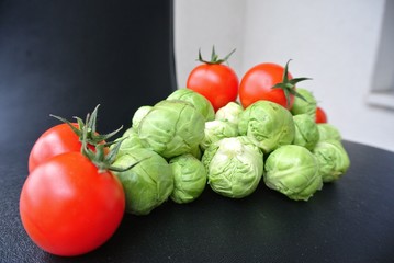 Pile of fresh green raw Brussels sprouts and red cherry tomatoes on the black table. Healthy/clean eating concept; healthy, fresh, organic, unprocessed food; paleo diet.