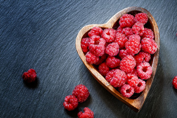 Fresh raspberries in a bowl in the shape of a heart on a dark ba