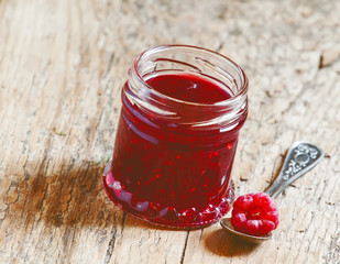 Raspberry jam in a jar and raspberries in a spoon on old wooden