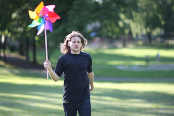 Young man with a colorful pinwheel in hand running through a park