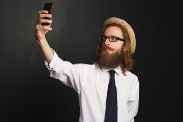 Hipster businessman with glasses and hat taking self portraits with his smartphone