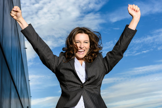 Young Business Woman Is Jumping For Joy In Front Of Blue Cloudy Sky