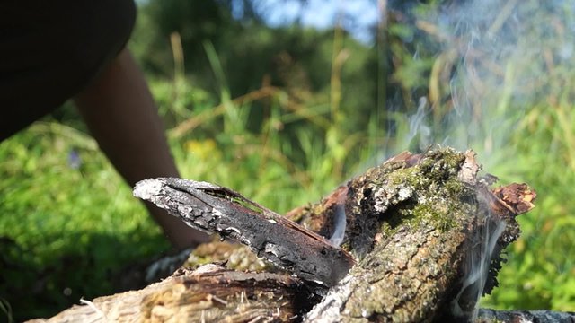Man fan the flames of the fire. Video with sound. You can hear the crackle of twigs, sound fanning the flames, the birds singing, the sound of the river.