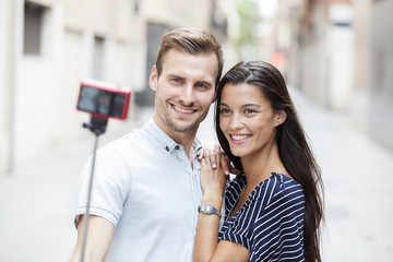 cheerful young couple making a selfie with a smartphone and selfie stick