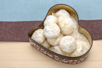 Homemade cookies in powdered sugar in a tin box in the shape of a heart on a cotton napkin striped
