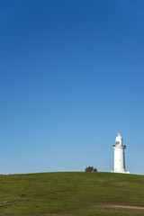 Macquarie Lighthouse on the horizon with green field and blue sky