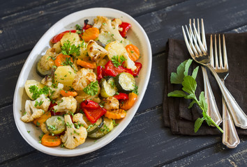 roasted vegetables - zucchini, cauliflower, potatoes, carrots, onions, peppers, on an oval dish on dark wooden background
