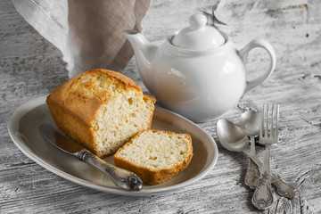 simple cake on an oval platter, a teapot and silver cutlery on a light wooden background
