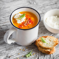 pumpkin soup served in an enamel mug with cream and paprika on a light wooden background