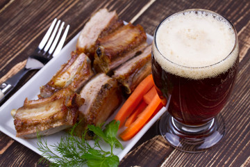 Glass Of Beer And Pork Ribs With Carrot On Wooden Background