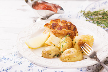 Delicious dinner: baked potatoes with thyme and cutlets, served with spicy tomato sauce. Selective focus