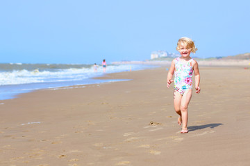 Fototapeta na wymiar Cute active child playing on sandy beach. Happy little girl enjoying summer holidays on a sunny day. Family with young kids on vacation at the North Sea coast.