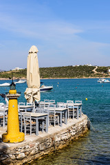 Traditional Greek taverna on the seafront on the beach - bright chairs and table, Alyki village, Paros island, Cyclades, Greece.