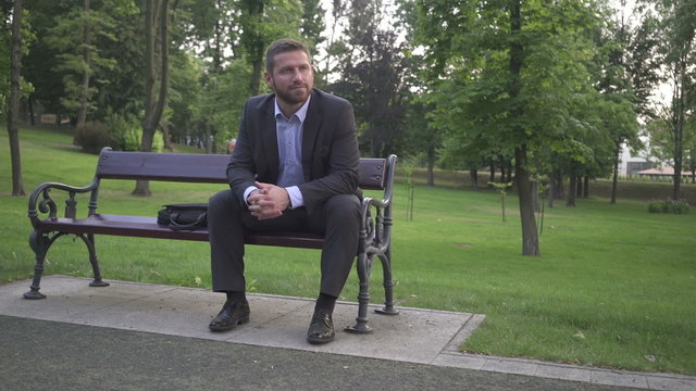 Businessman sitting and looking round, sitting on wood bench.
