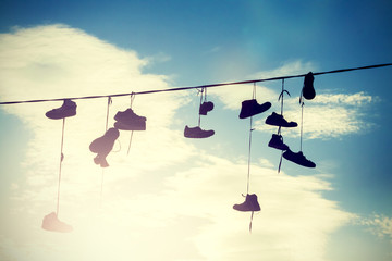 Instagram style silhouettes of shoes hanging on cable at sunset.