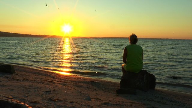 A woman sitting on a stone looking at the sunrise over the sea